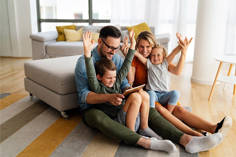 Life Insurance - Family Smiling and Sitting on the Floor in Their Living Room While Looking at a Tablet